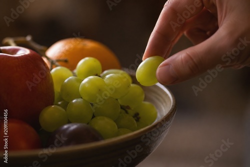 A single green grape being taken from a full fruit bowl, soft light.