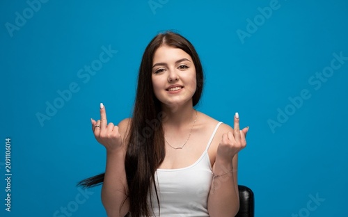 Young brunette woman smiling, gesturing middle fingers, expressing rebellion and disrespect on blue background