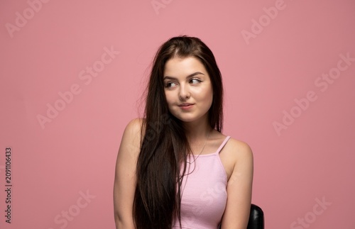 Bild auf Leinwand Young brunette woman looking sideways with shy smile on pink background, feeling