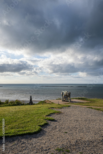 Panoramic sunset view over Gold Beach and Arromanches-les-Bains from the cliff in Normandy, France, featuring World War II remnants and cloudy sky.