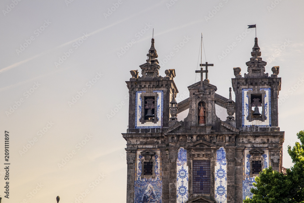 Fototapeta premium Plano detalle de las torres campanario de la barroca Iglesia de San Ildefonso, decorada con tradicionales azulejos azules y blancos bajo una suave luz de atardecer en Oporto, Portugal.