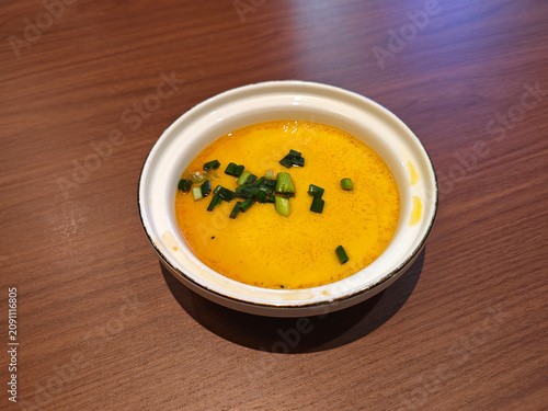 A white bowl of smooth, golden steamed egg custard, garnished with fresh chopped green scallions