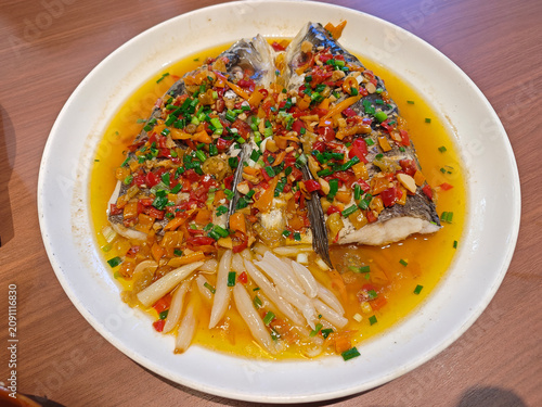 A steaming plate of Hunan chopped pepper fish head, garnished with vibrant red chilis, scallions