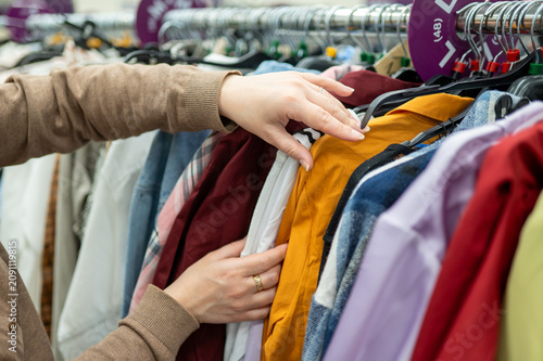 Woman hands choosing clothes on rack in second hand or stock store