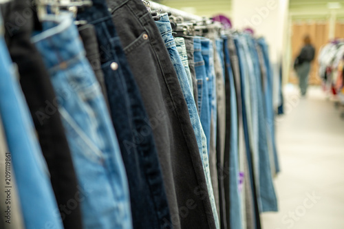 Row of blue and black denim jeans on hangers in stock or second hand clothing store