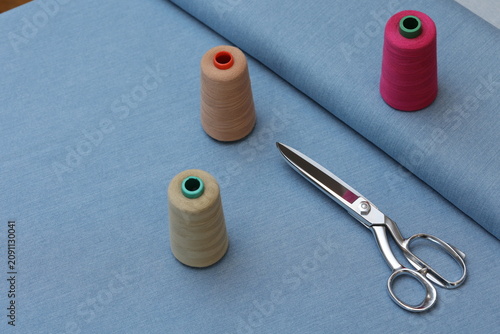 Foto Professional tailor scissors and colorful thread spools arranged on a blue denim fabric background