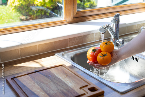 Obraz na plátně Hand rinsing fresh tomatoes under running water before healthy home cooking