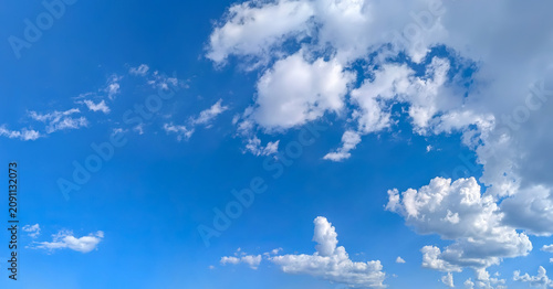 A high-resolution image showcasing a vibrant blue sky filled with scattered white cumulus clouds. The natural daylight highlights the soft textures of the clouds.