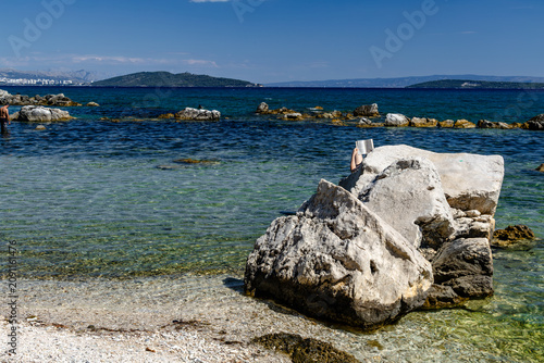Studying for retake exams on the Adriatic Sea, reading books on a pebble beach in Kastel, Croatia. A student studies for a retake exam during the summer holidays.