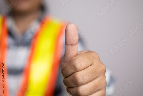 Construction worker giving a thumbs up gesture while wearing a reflective safety vest, representing workplace safety, confidence, approval, and successful project completion.