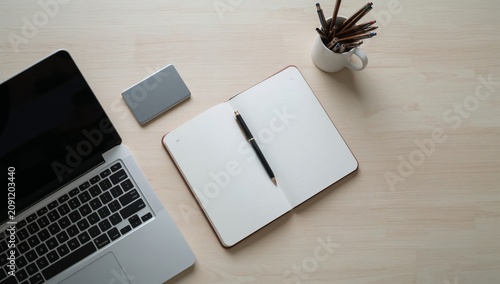 Working on a Laptop With an Open Notebook and a Cup of Pens on a Wooden Table