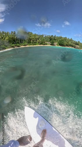 VERTICAL, SLOW MOTION, FPV: Surfing along clean tropical wave with view of shoreline covered with palm trees. Spraying water, sun, turquoise sea and riding surfboard at a remote Indonesian surf spot.