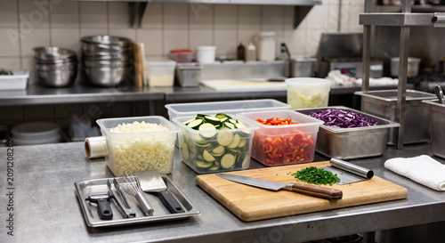 Restaurant kitchen prep counter with colorful vegetables, cutting boards, knives, towels, and cookware arranged for food preparation
