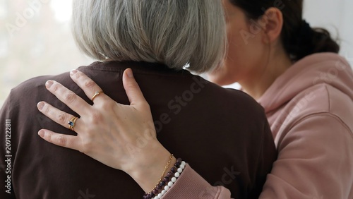 Young woman embracing elderly lady with care showing love and support in warm close human contact.