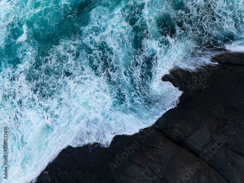 Turquoise ocean waves crashing against dark coastal rocks