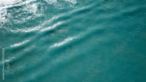 Abstract aerial view of turquoise ocean waves crashing with white foam and deep blue water