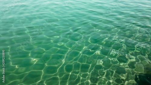 Calm ocean surface with shimmering sunlight patterns reflecting on the clear green water