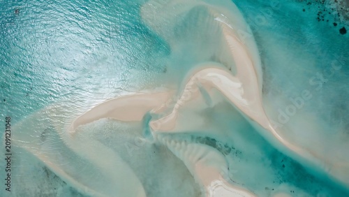 Aerial view of shallow turquoise ocean water revealing abstract sandbars and underwater patterns