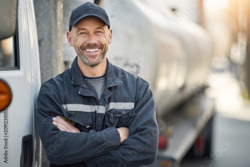Portrait of a smiling propane technician in uniform standing beside a propane tank or truck, neutral and uncluttered background, warm approachable tone. 