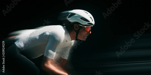 Professional cyclist in motion, wearing a white helmet and sunglasses, focused on the race