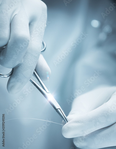 Close up of surgeon hands in sterile medical gloves using stainless steel needle holder and suture