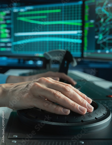 Operator hand using a large dial jog wheel console with background digital analytics graph screen