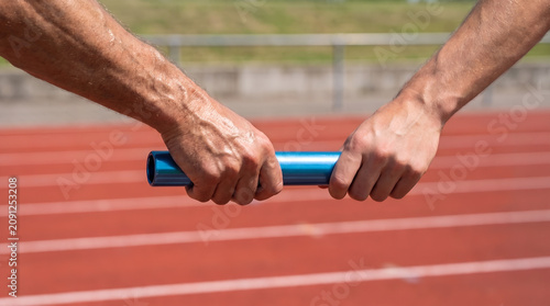 Close up of track and field athletes passing the relay baton during a race with athletes handover competition teamwork athletics training exercise cooperation