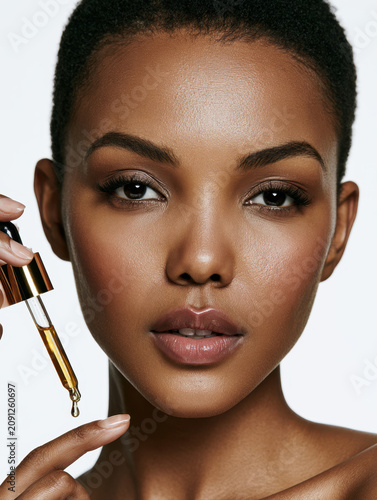 beautiful black african american woman applying cosmetic serum oil with a dropper closeup face of young female with perfect clean skin health care cosmetology dermatological treatment copy space