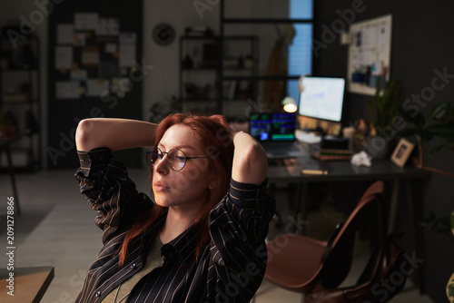 Young adult Caucasian businesswoman leaning back in office chair, pausing during computer work and reflecting on workload. Useful for burnout, remote work, stress management marketing