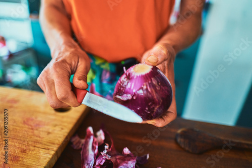 Woman peeling a red onion with a knife - home cooking close-up