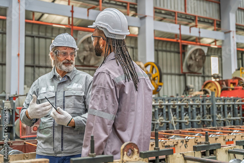 Two industrial workers inspecting machinery in a factory. Teamwork, precision, and safety gear highlight professional collaboration in metal production and mechanical maintenance.