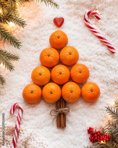 Mandarin Orange Christmas Tree Holiday Flat Lay Mandarin oranges arranged as a Christmas tree with cinnamon trunk, candy canes, evergreens, and berries on cozy white fabric