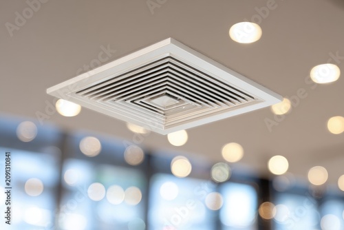 Close-up of a square ceiling air vent, surrounded by recessed lights and blurred background