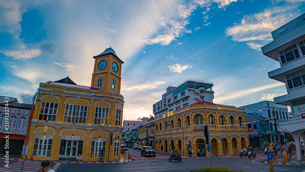 Fototapeta premium Twilight Time Lapse at the Iconic Phuket Clock Tower. Beautiful evening cityscape showcasing famous clock tower with dramatic pink and purple sunset clouds above the historic district of Phuket city