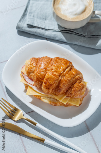 A golden croissant sandwich with ham and cheese on a white plate on a tile background