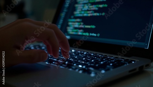 Person Types Code on Laptop While Sitting in Dimly Lit Room at Night
