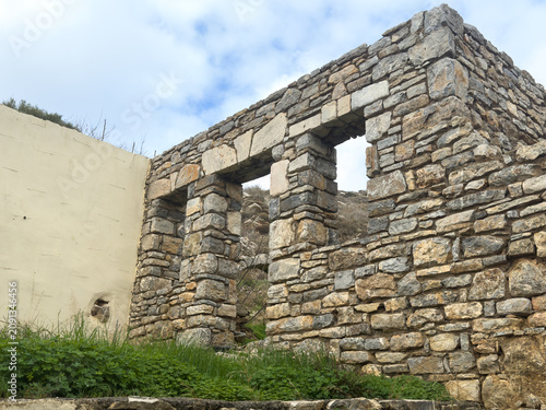 Ruins of an abandoned traditional stone building in Greece against a cloudy blue sky, capturing historic rustic Mediterranean architecture and heritage.