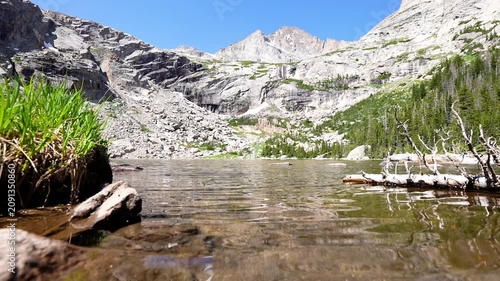 wide shot of beautiful rocky mountain Black Lake in the RMNP colorado rockies Rocky Mountain National Park with reflection on clear glacial water and cloudless blue sky and grass shore