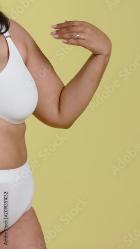 Vertical video: Moving hand, model extending arm, rotating at yellow studio showing white lingerie