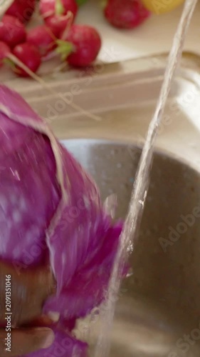 Vertical video: Turning on faucet, hands rinsing, peeling red cabbage for prep over sink, colander