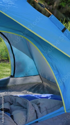 Vertical video: Panning camera up from low-angle, revealing blue tent on lawn, grey bag and pad