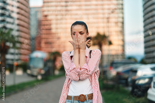 Fotografía A distressed woman on a city street covers her face with her hands, conveying anxiety, surprise, and vulnerability in a casual, everyday moment