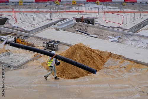 construction site worker carrying black plastic pipework on building site