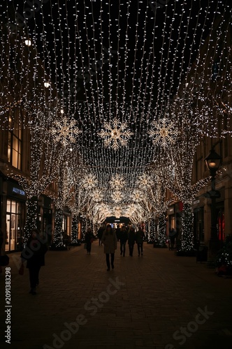 Shoppers Walk Under Bright Lights and Decorations at a Festive Street in Winter