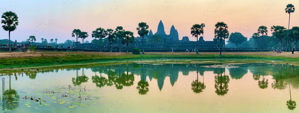 Obraz premium Siem Reap, Cambodia - February 20, 2020: Wide Panoramic View of Angkor Wat Temple and Its Reflection in a Lily Pad Pond at Sunset