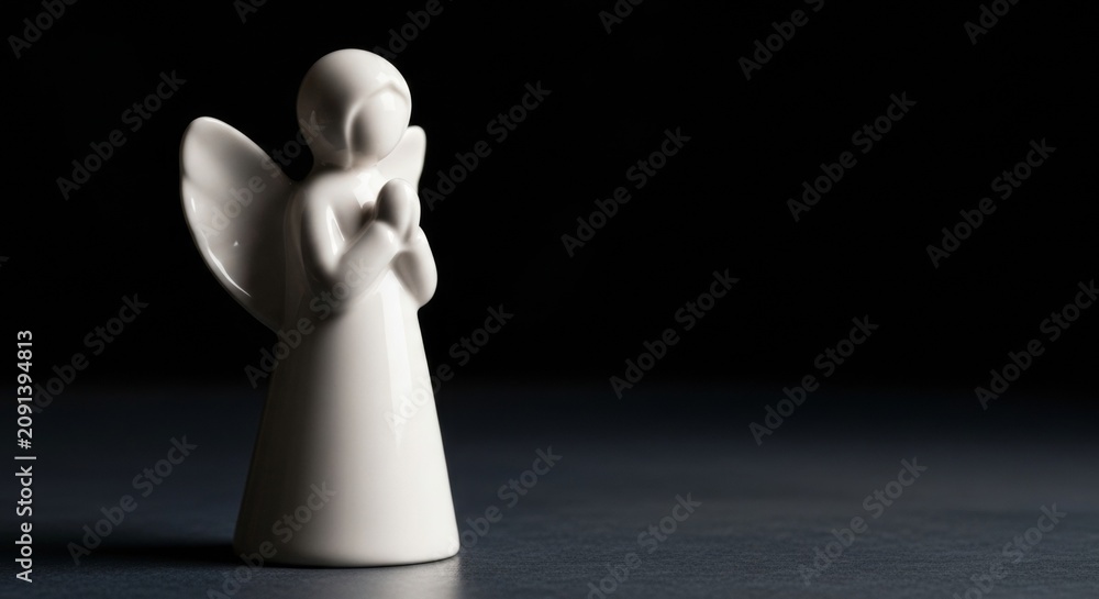 Obraz premium Minimalist white angel figurine with folded hands on dark polished surface, elegant lighting, serene home decor