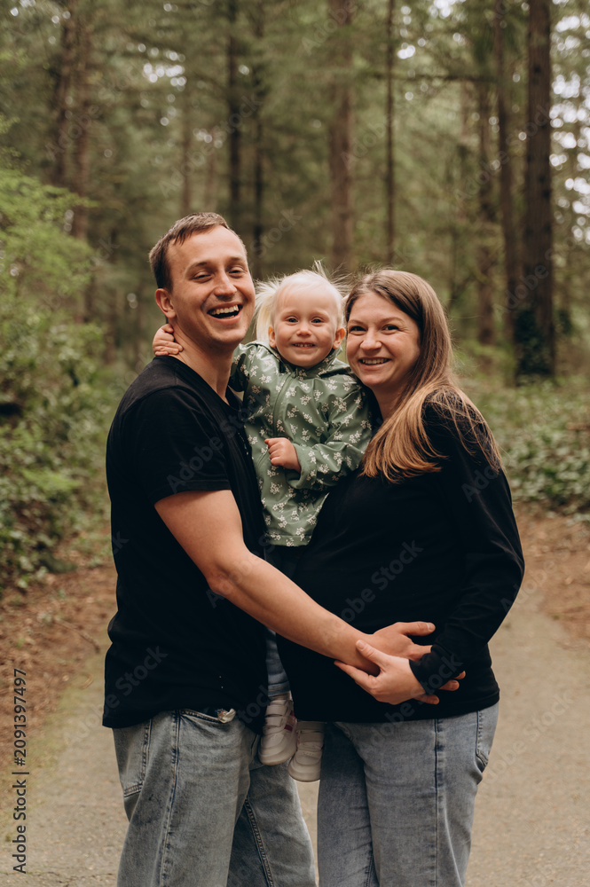 Fototapeta premium A warm family walk along a forest path. Parents are spending time with their child amidst tall trees and nature.