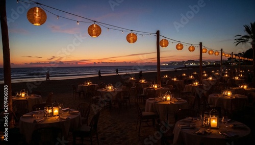 Dinner Setup Along Beach During Sunset With Lanterns Strung Across Tables and...