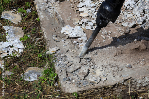 Fotografie A hydraulic jackhammer breaks an old concrete slab on an outdoor construction site