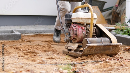 Foto Plate compactor working on sandy ground beside concrete curb during outdoor cons